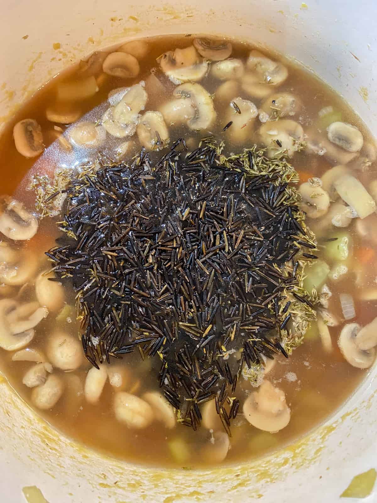 Pot with sauteed vegetables and broth, with dry wild rice just added.