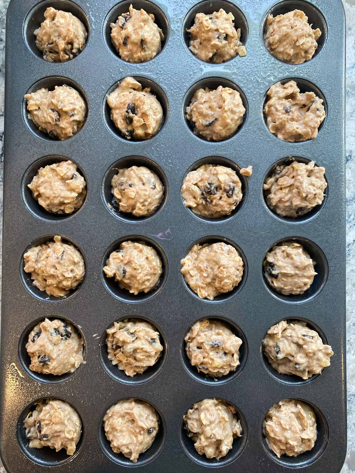 Muffin batter scooped into muffin baking pan.