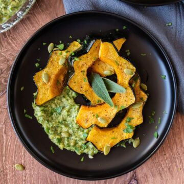 Slices of roasted acorn squash on a plate over sage pesto with pepitas.