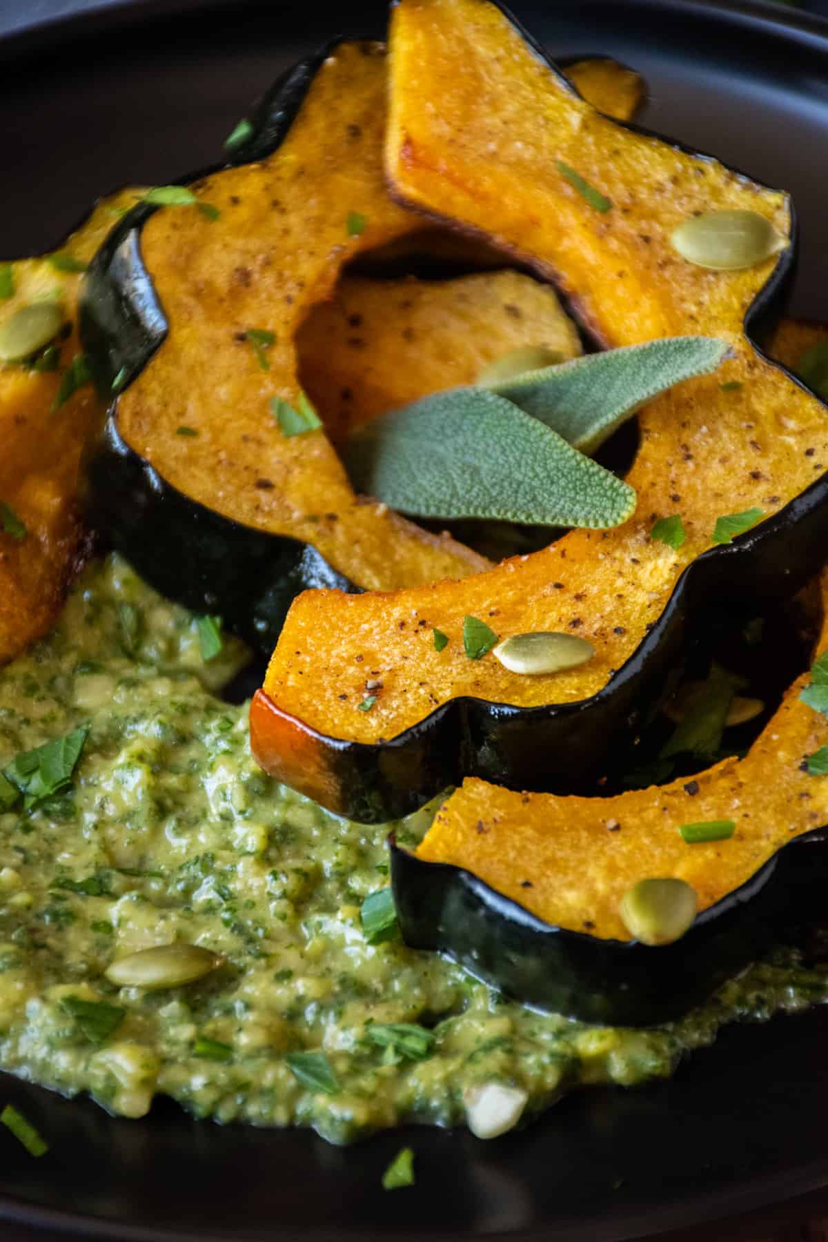 Slices of roasted acorn squash on a plate over sage pesto with pepitas.