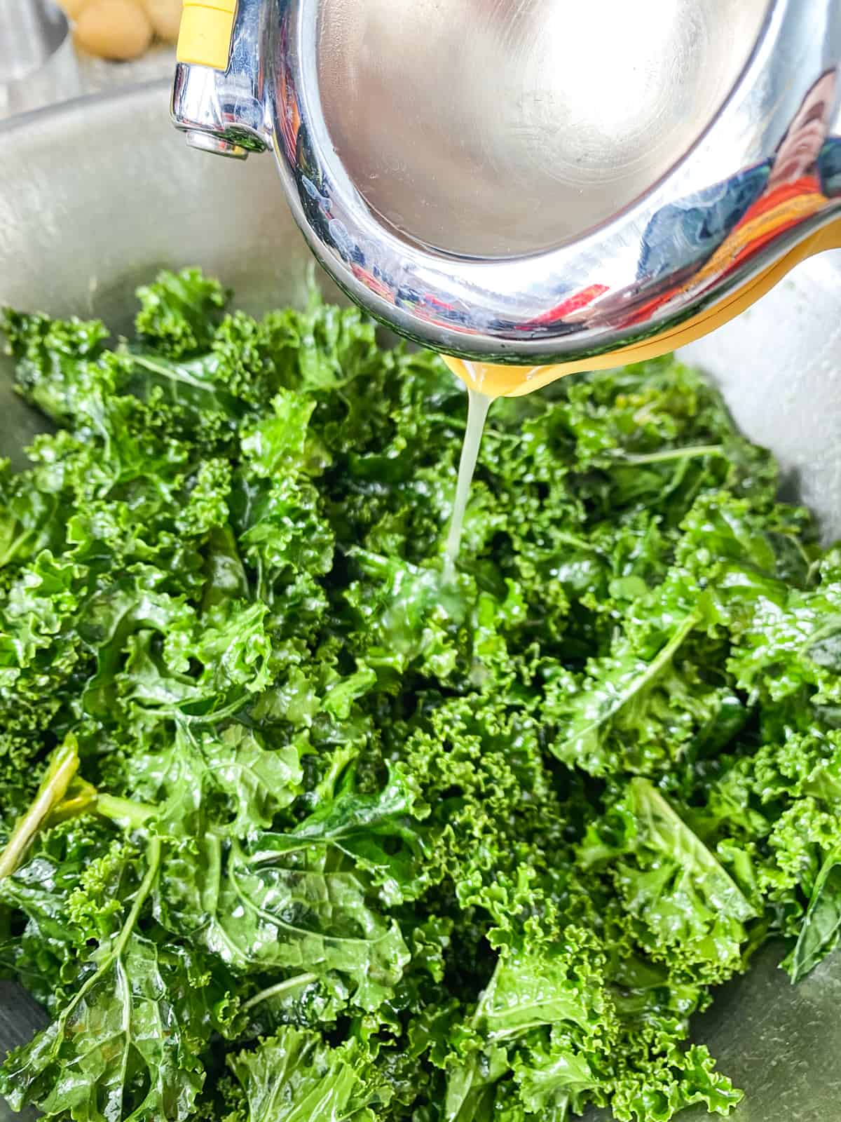Bowl of massaged kale, with orange juice being poured into it.
