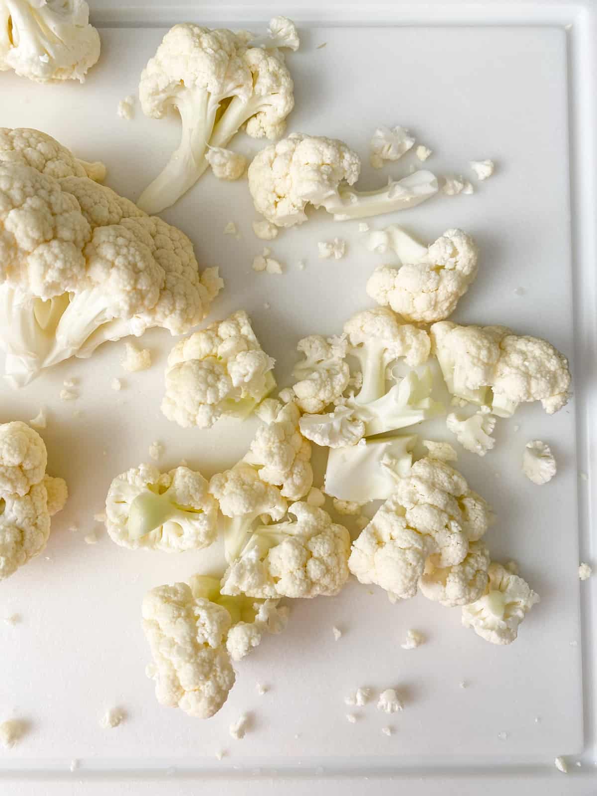 Cauliflower cut into small florets on a cutting board.
