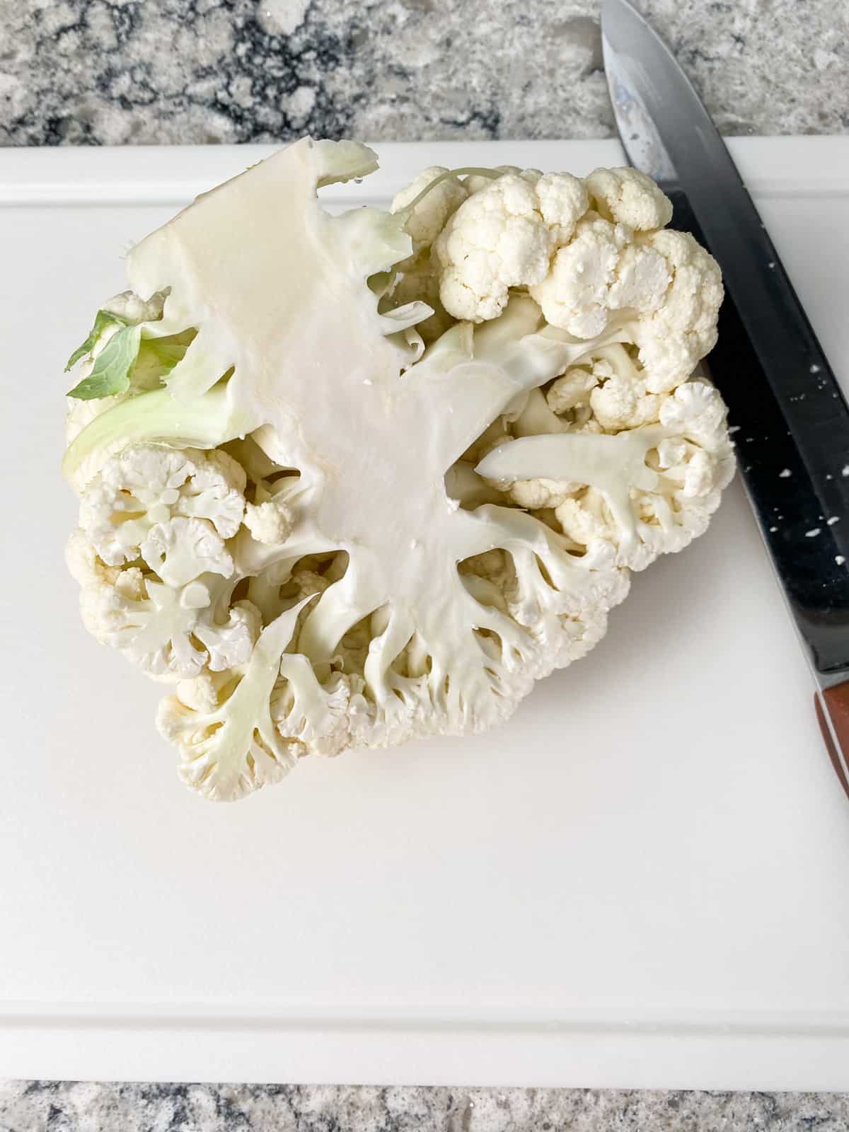 Half of a head of cauliflower on a cutting board.
