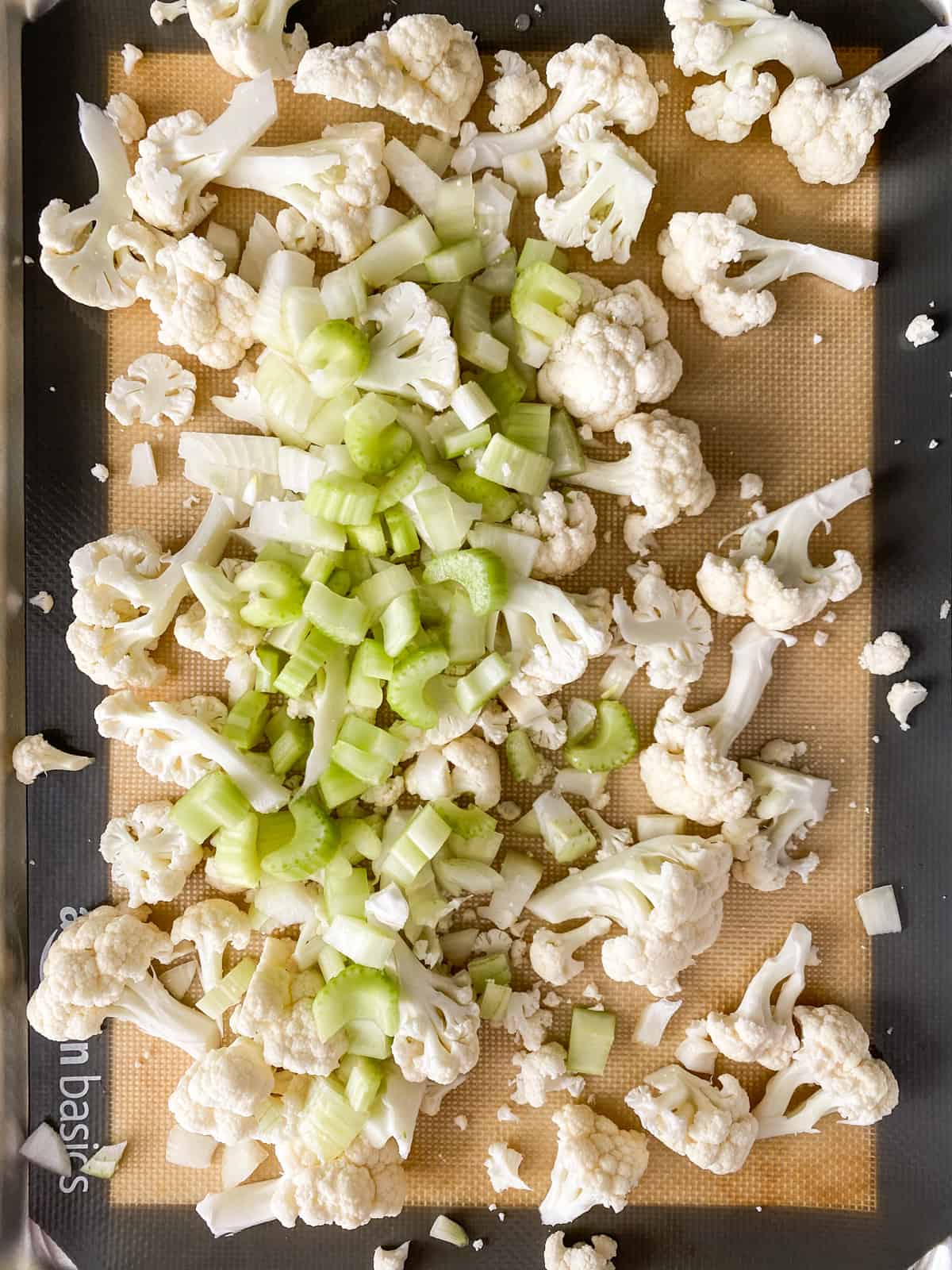 Chopped cauliflower, celery, and onions on a baking sheet.