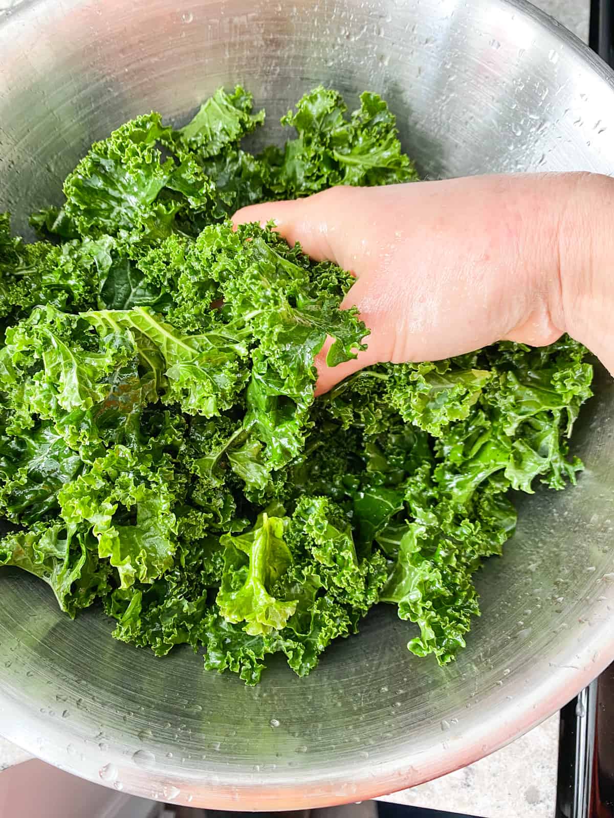 Kale in a large bowl, with a hand massaging it.