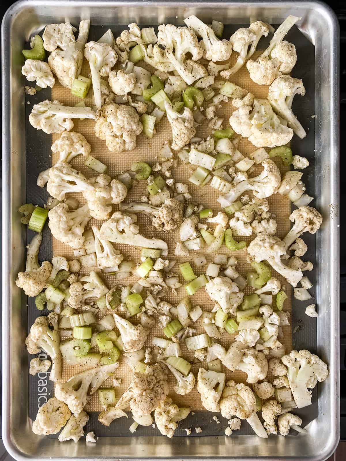 Chopped vegetables tossed with herbs and oil, on a baking sheet.