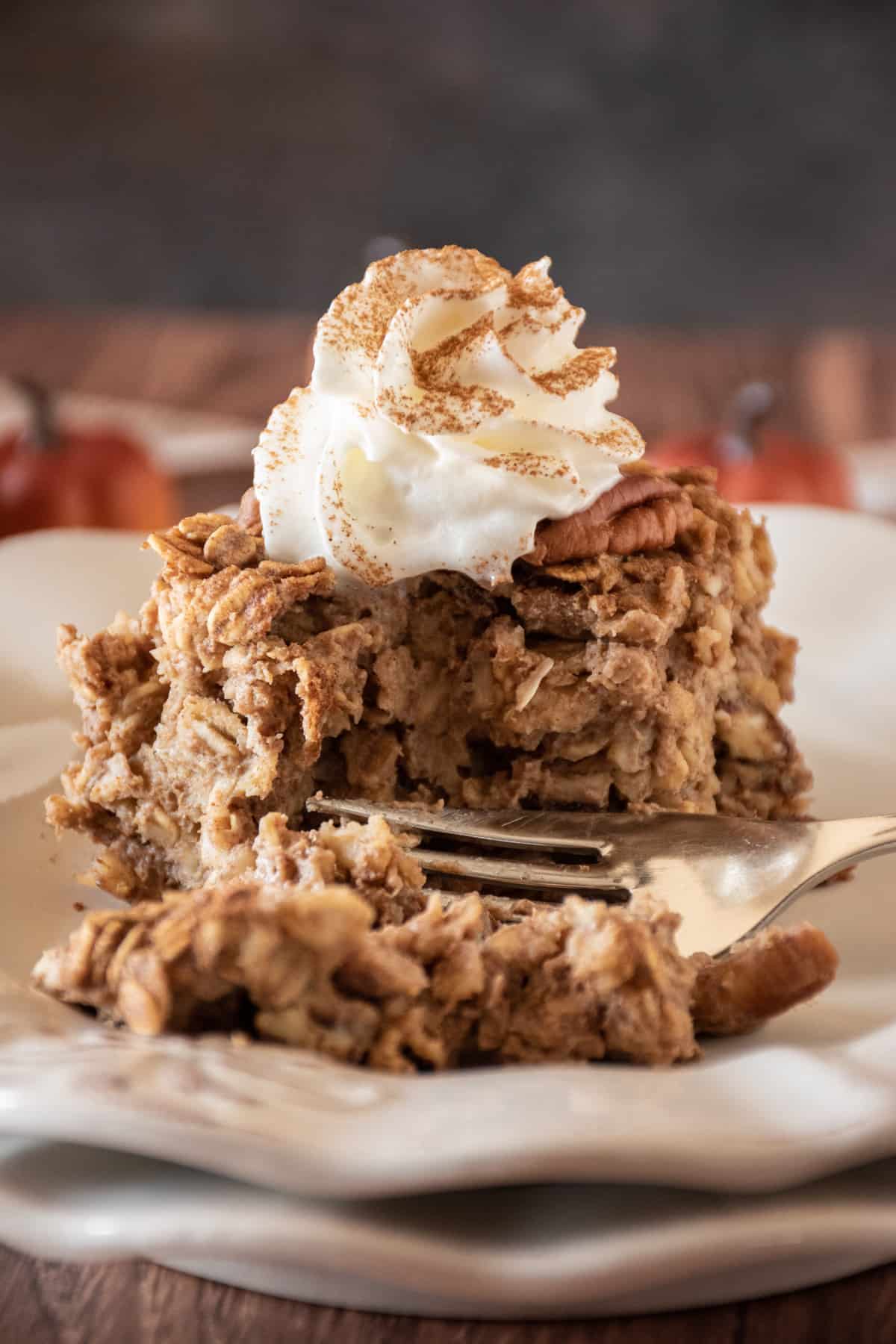 Square of pecan pie baked oatmeal on a plate, topped with whipped cream and a dusting of cinnamon.