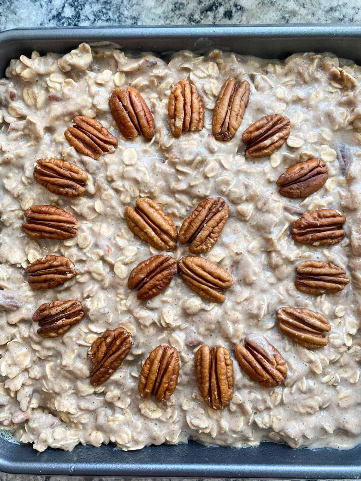 Ingredients poured into a baking pan, with pecan halves arranged decoratively on top, ready to go into the oven.