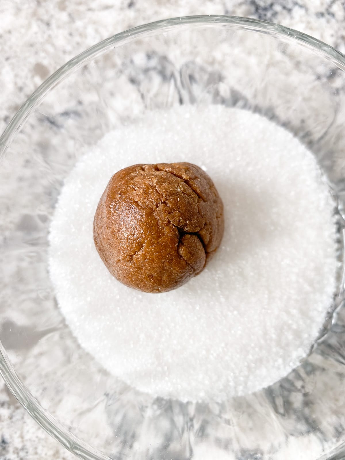 Cookie dough, rolled into a ball, in a small dish of granulated sugar.