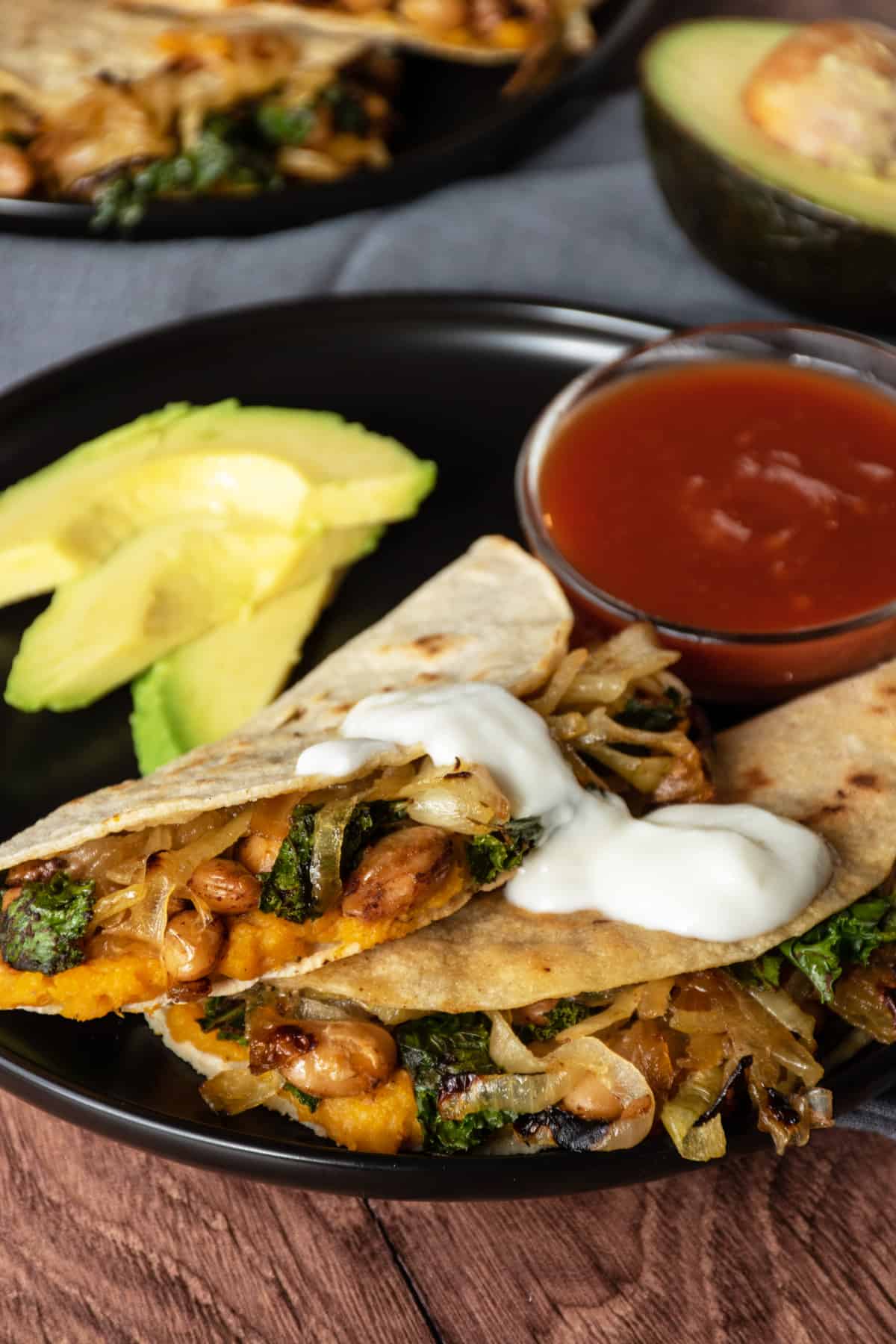 Two quesadillas on a plate, with a bowl of salsa, garnished with avocado slices and a dollop of plain unsweetened yogurt, instead of sour cream.