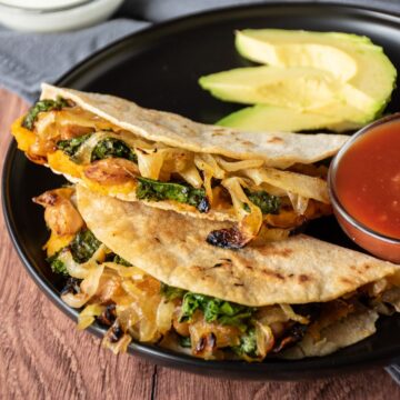 Two quesadillas on a plate, with a bowl of salsa, garnished with avocado slices.
