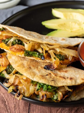 Two quesadillas on a plate, with a bowl of salsa, garnished with avocado slices.