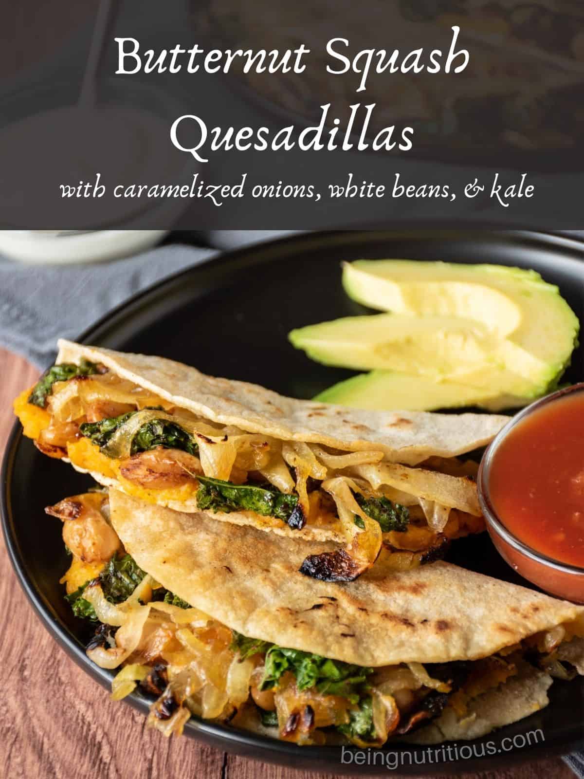 Two quesadillas on a plate, with a bowl of salsa, garnished with avocado slices. Text overlay: Butternut squash quesadillas with caramelized onions, white beans, and kale.
