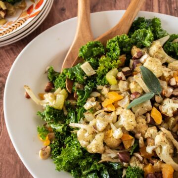 Large serving dish with kale and cauliflower on it, with serving utensils.