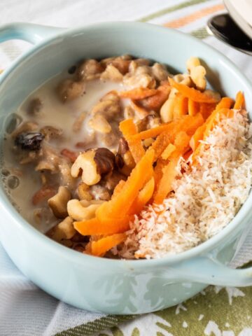Oatmeal in a small bowl, garnished with walnuts, shredded carrots, and toasted coconut.