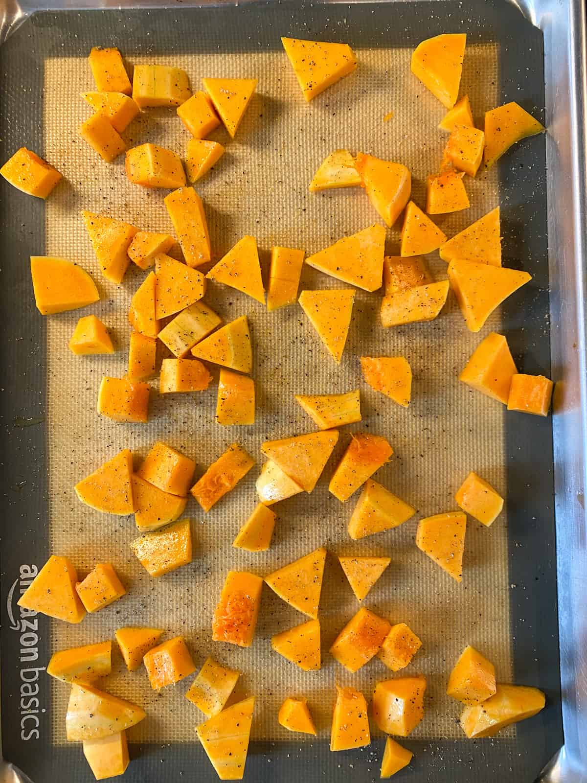 Raw butternut squash cubes, tossed with oil and pepper, on a baking sheet.