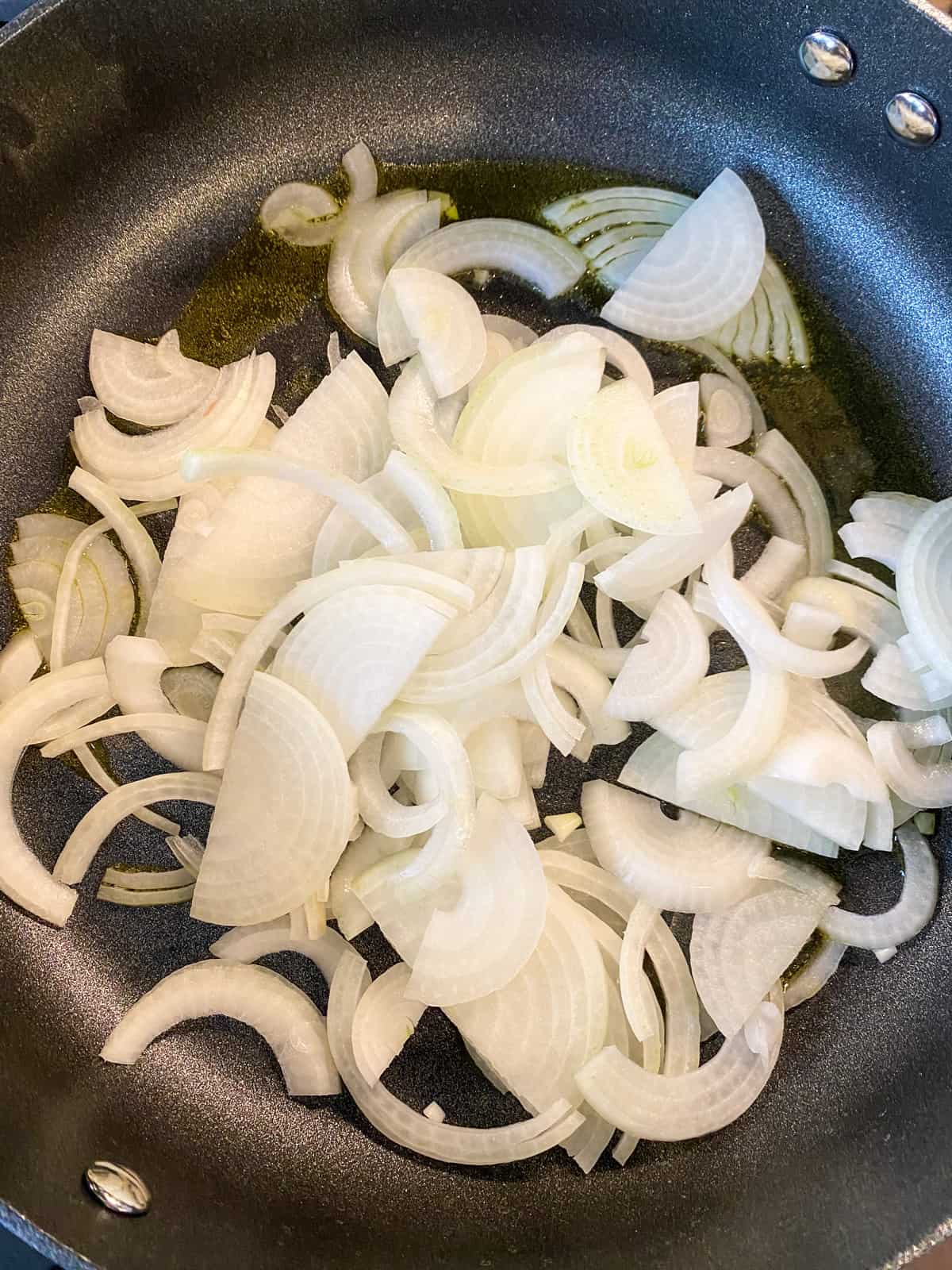 Sliced raw onions added to a skillet to sauté.
