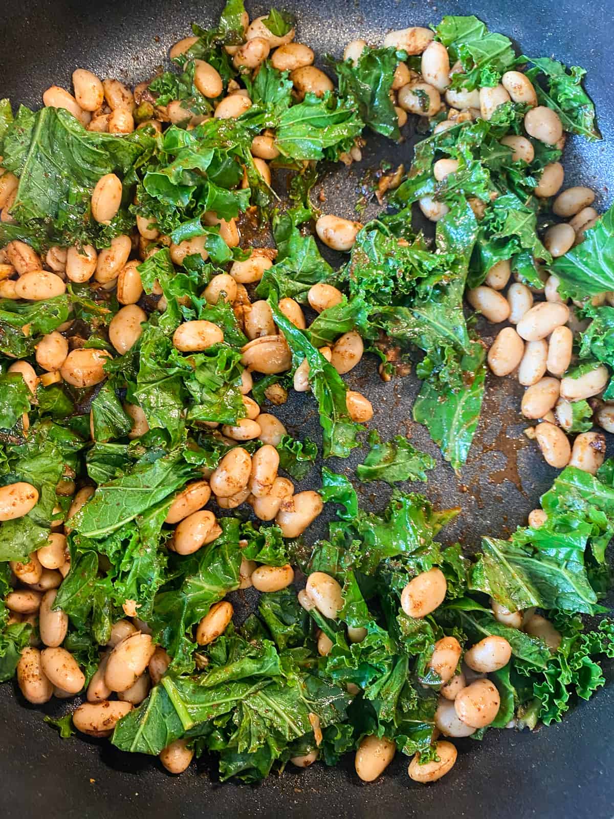 Finished white bean and kale mixture, in a skillet.