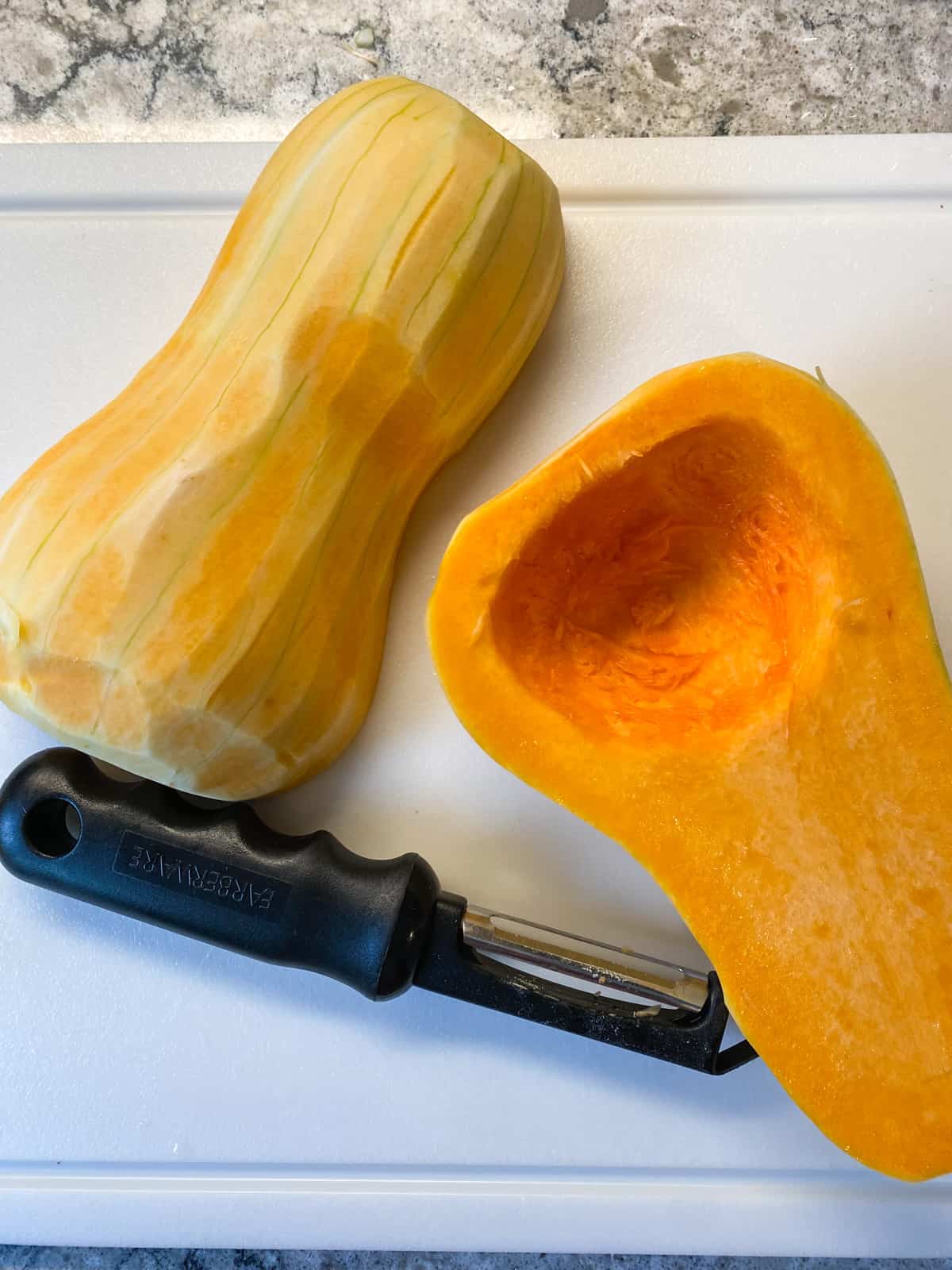 A butternut squash, peeled, halved, and seeded, on a cutting board.