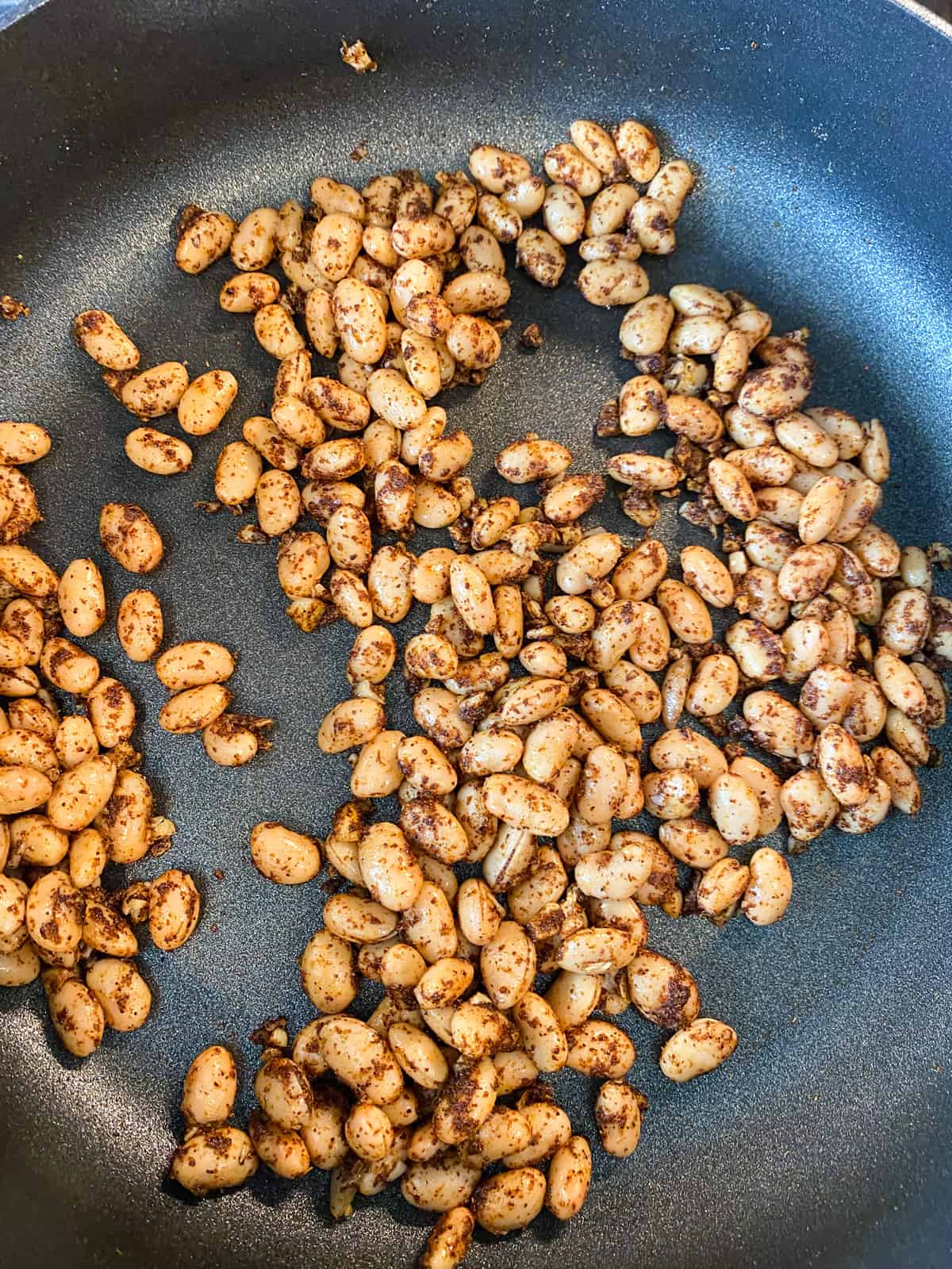 White beans sautéed in seasoning, in a skillet.