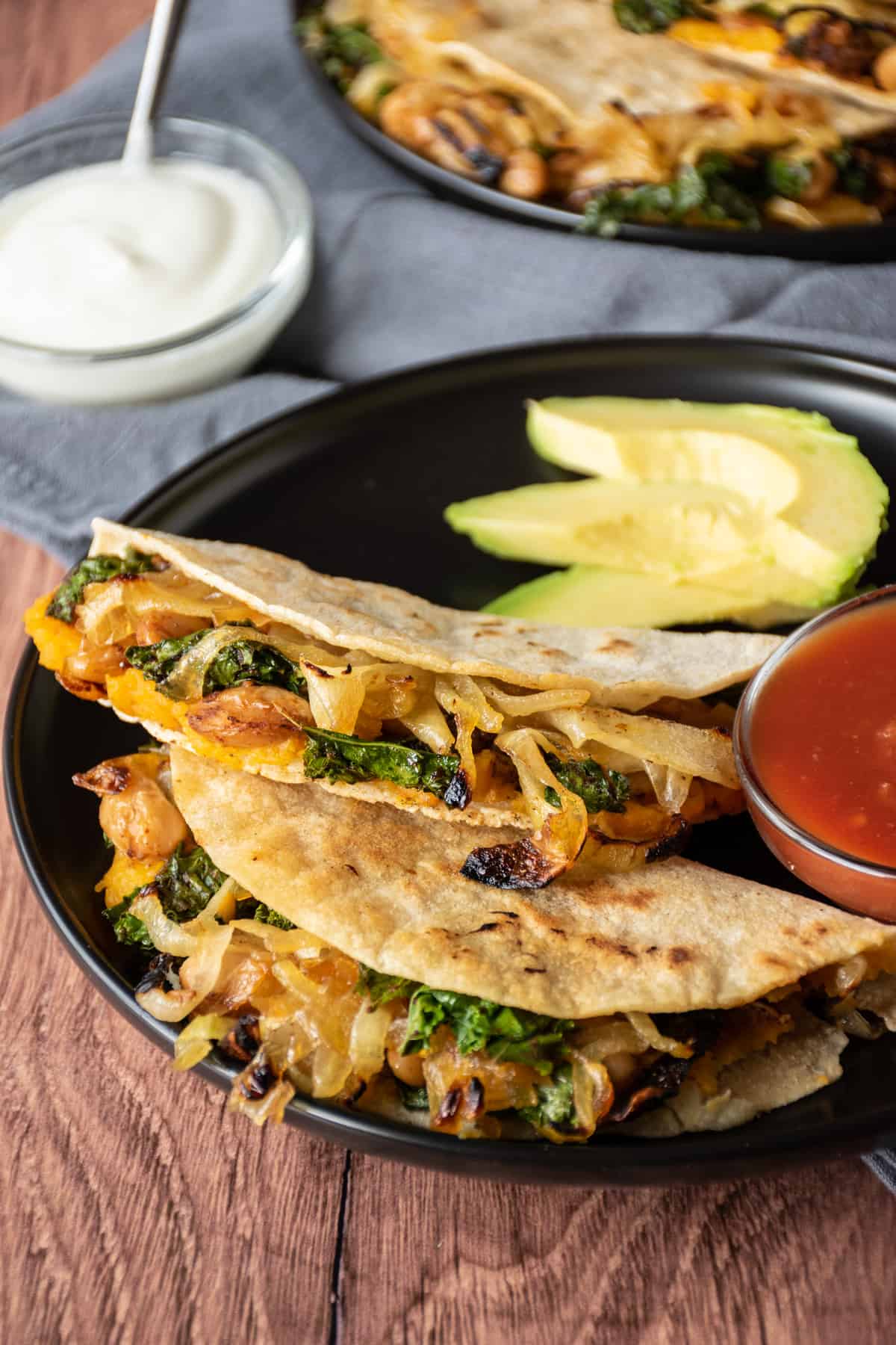 Two quesadillas on a plate, with a bowl of salsa, garnished with avocado slices.