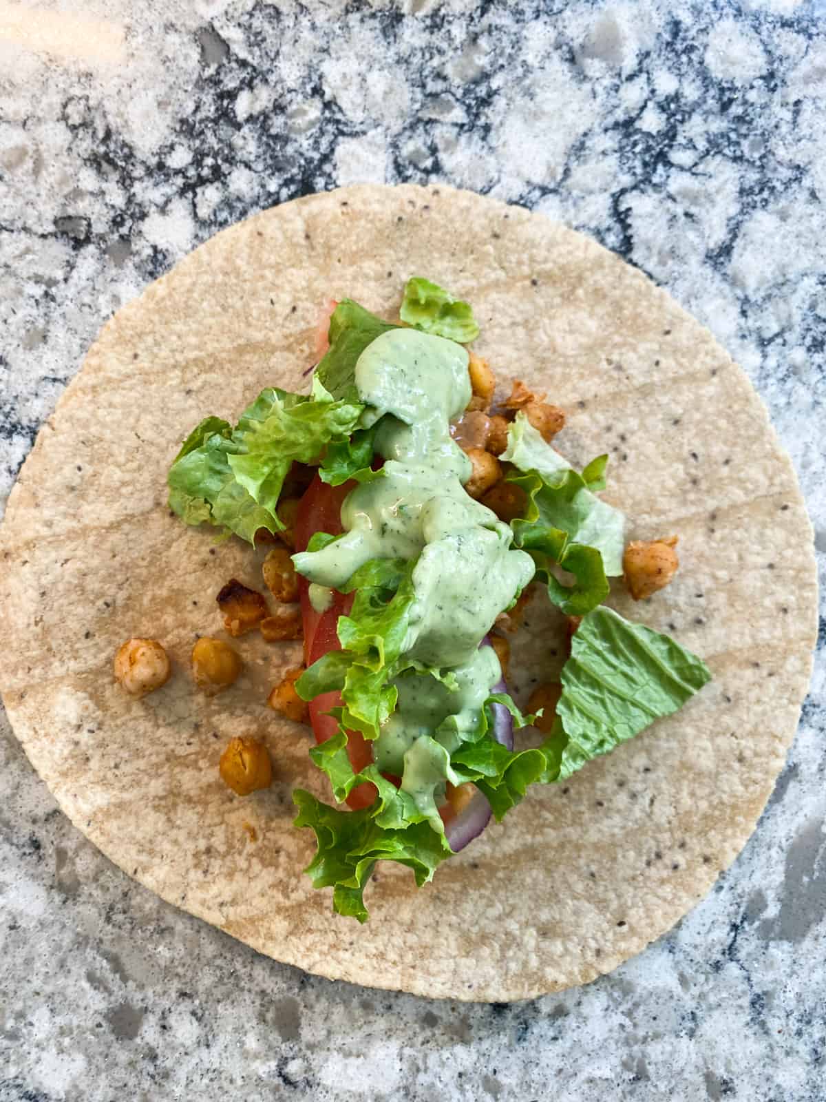Tortilla flat on the counter with all ingredients for buffalo chickpea wraps on it, ready to roll.