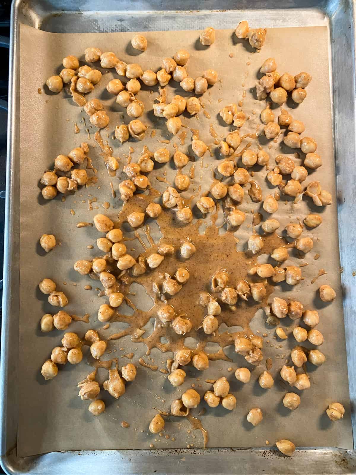 Buffalo sauce covered chickpeas on baking sheet, ready for baking.