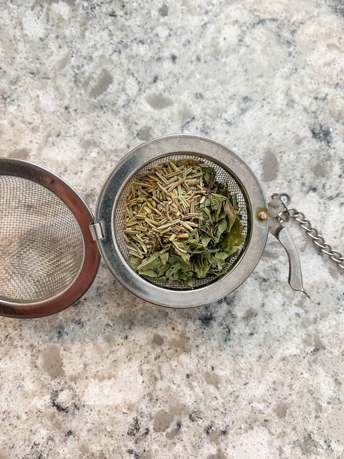 Dried rosemary and mint in a tea ball strainer.