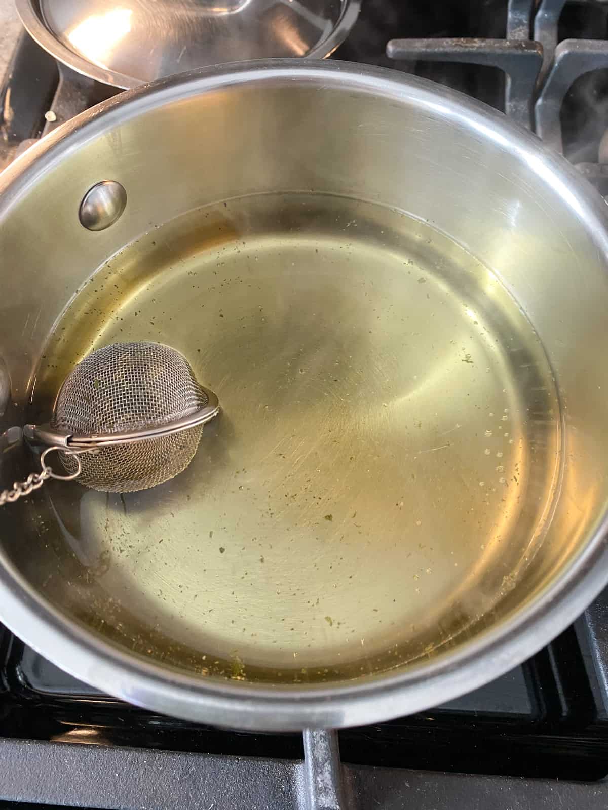 Hot water in a pot with a tea strainer ball in it, steeping.