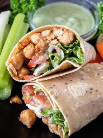 Wrap with chickpeas, lettuce, tomato and onion, cut in half, on a plate with celery and carrot sticks.