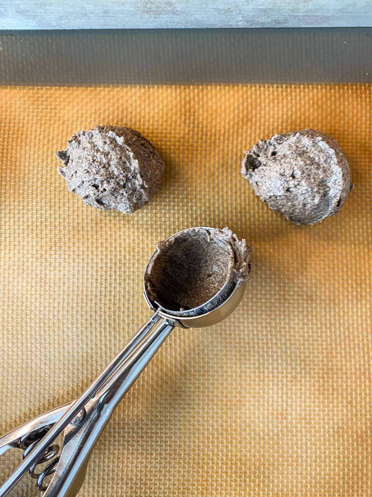 Biscuit batter scooped onto a baking sheet lined with a silicone baking mat, and the scoop visible in the frame.