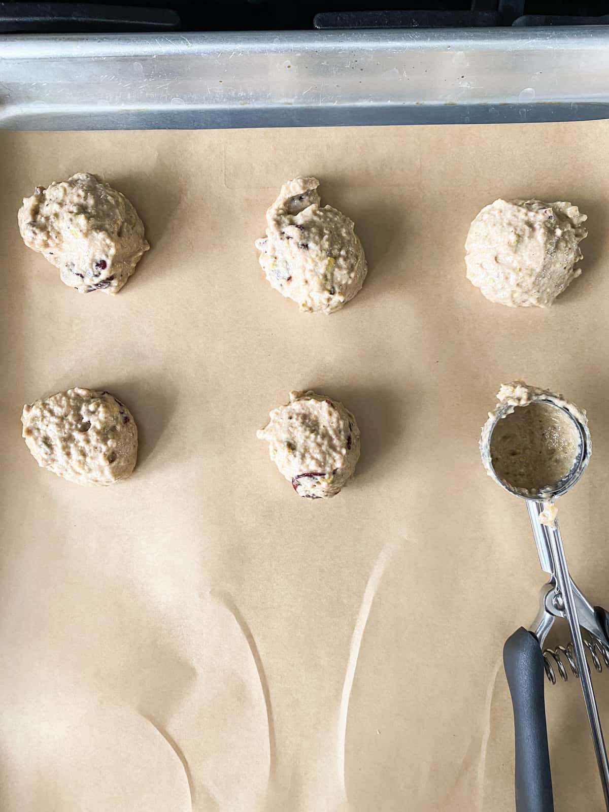 Cookie batter scooped onto a baking sheet, lined with parchment paper.