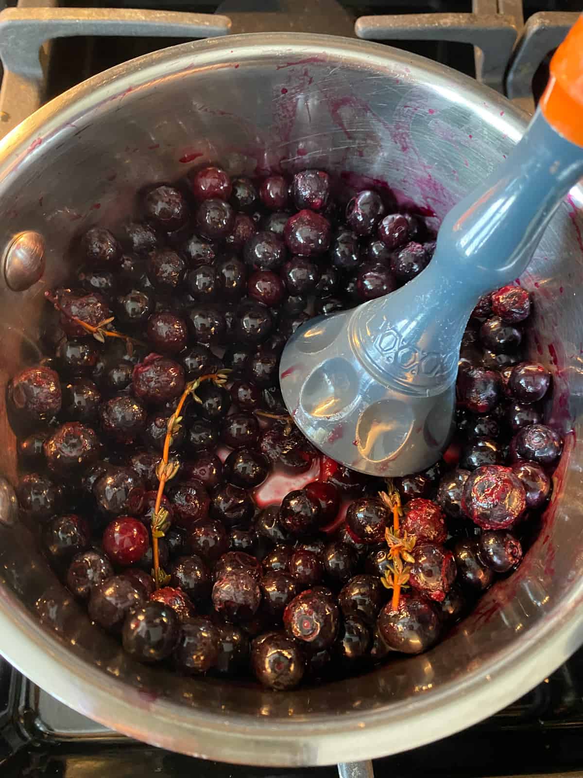 Small pot with frozen blueberries, sprigs of thyme, and a masher to mash the berries.