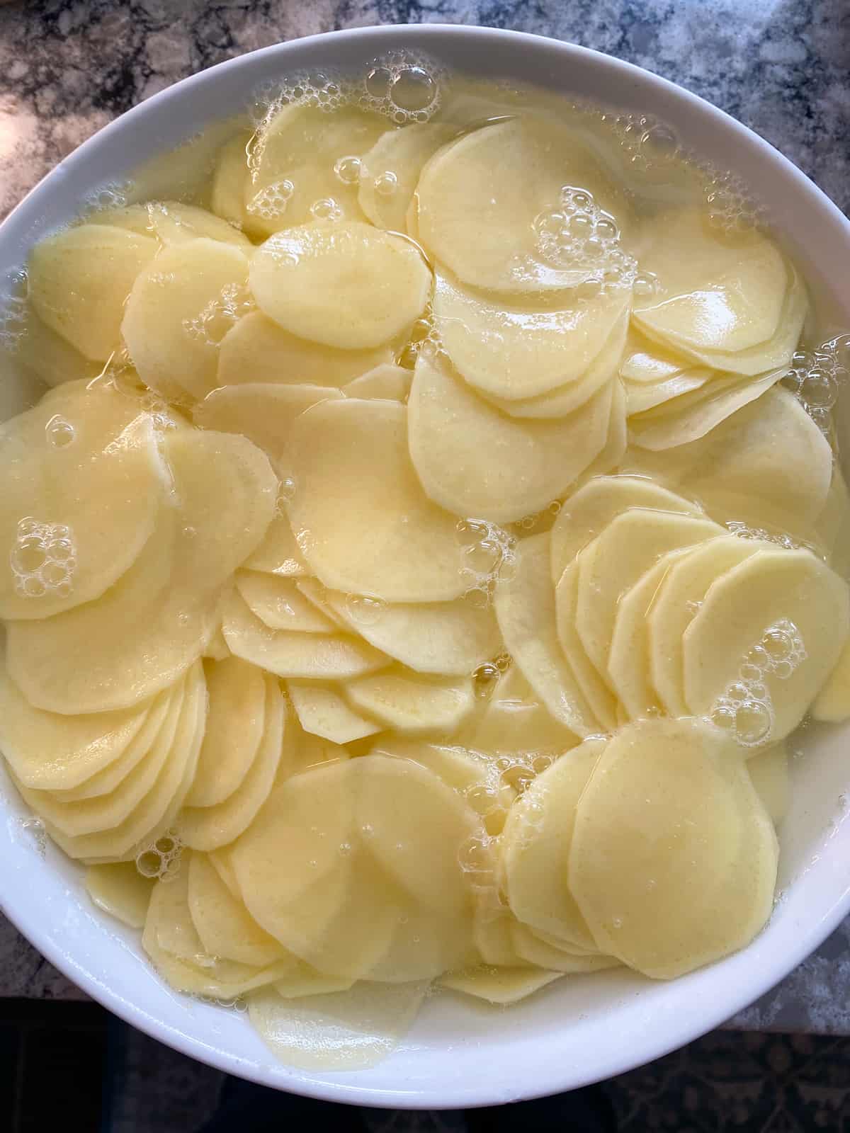 Sliced potatoes in a bowl, covered with water.