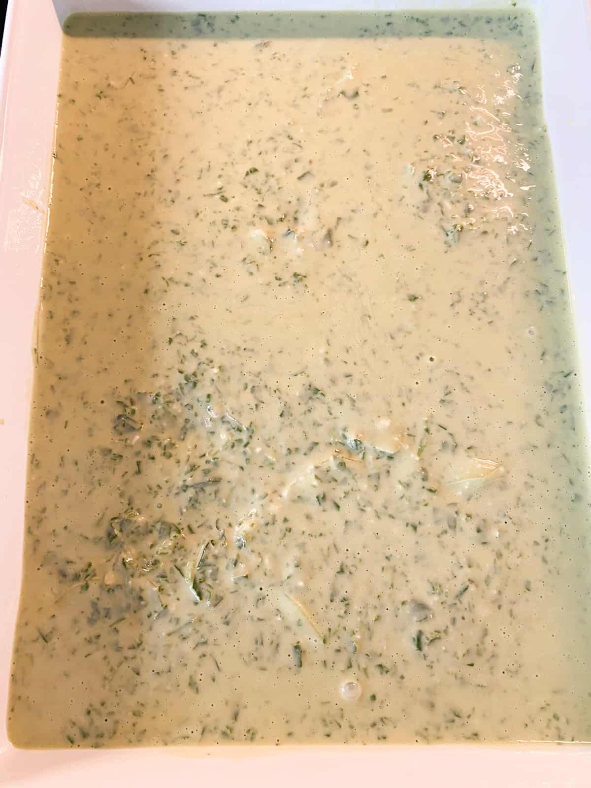 Pesto sauce poured over the potatoes in a baking dish.