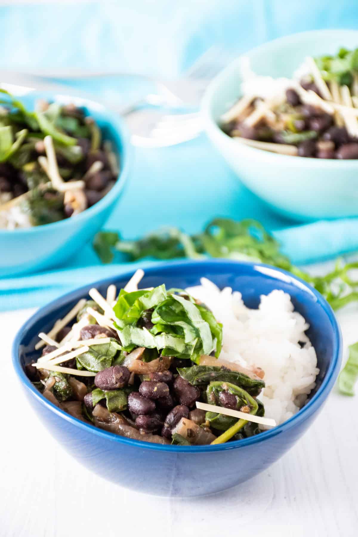Bowl of black beans and rice, garnished with fresh basil and shredded parmesan cheese. Two additional bowls in the background.
