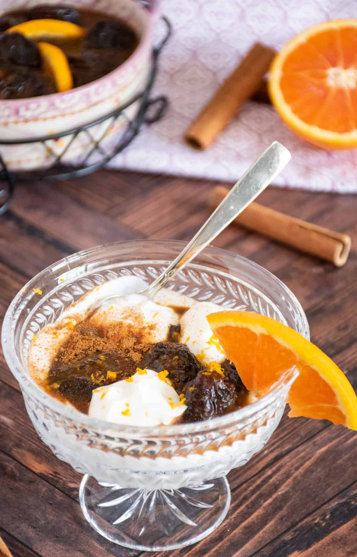 Small glass dish with yogurt and prune compote, garnished with an orange slice, cinnamon sprinkle, and orange zest.