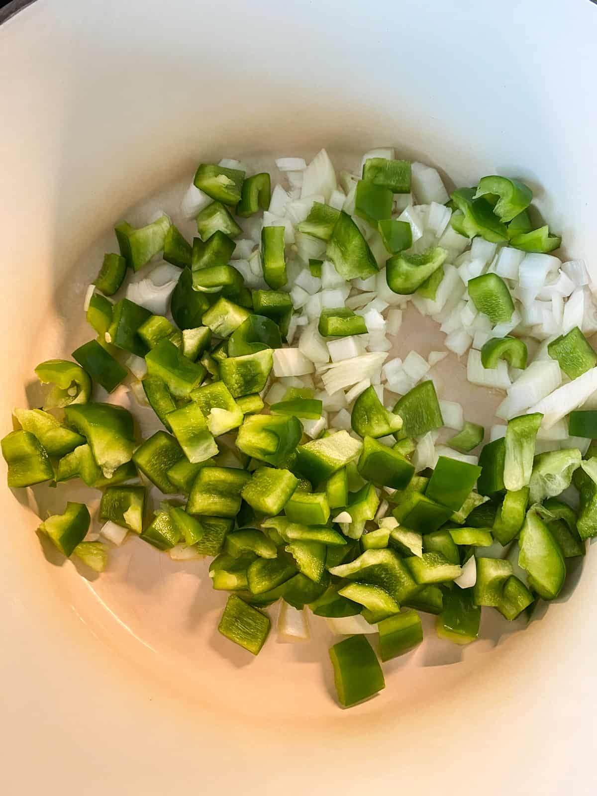 Chopped onions and peppers added to a pot to sauté.