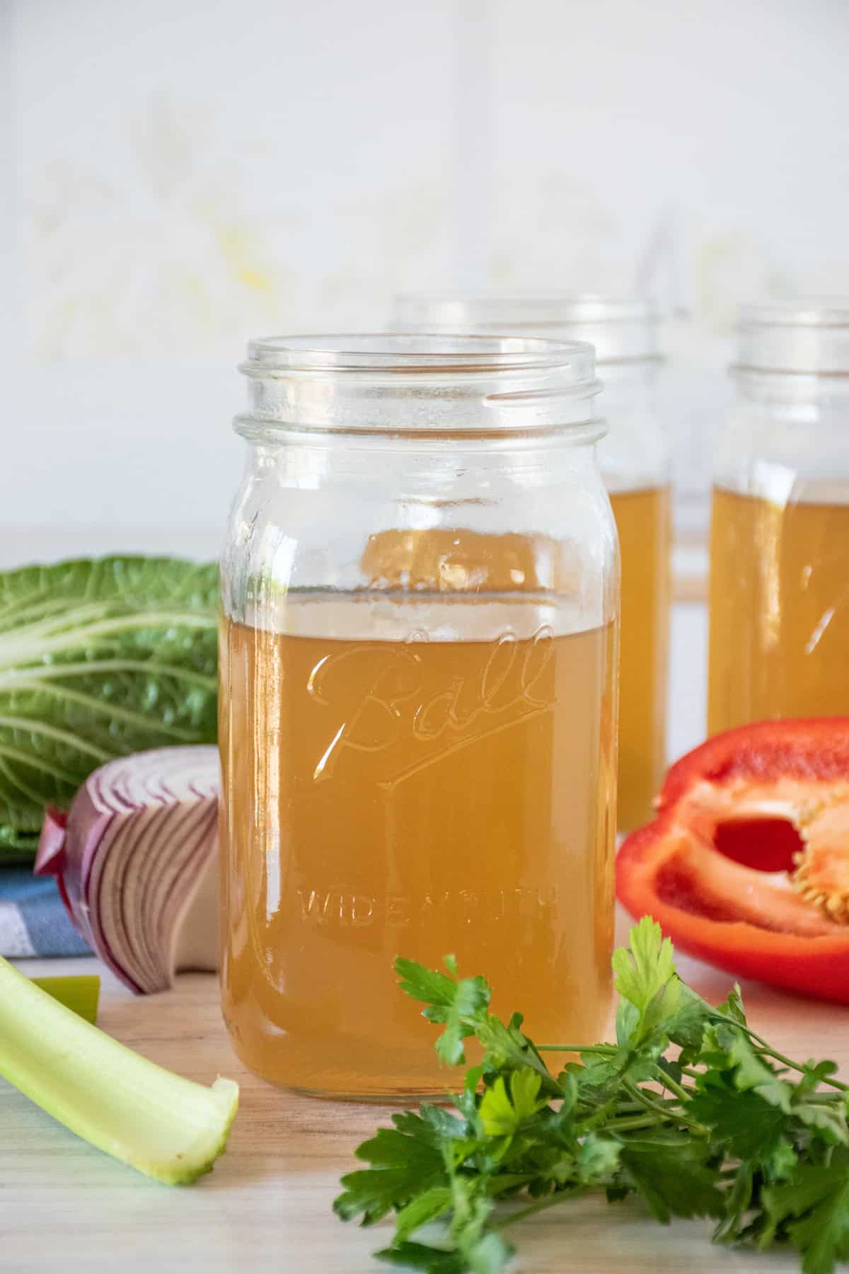 Vegetable stock in a mason jar, surrounded by fresh vegetables.
