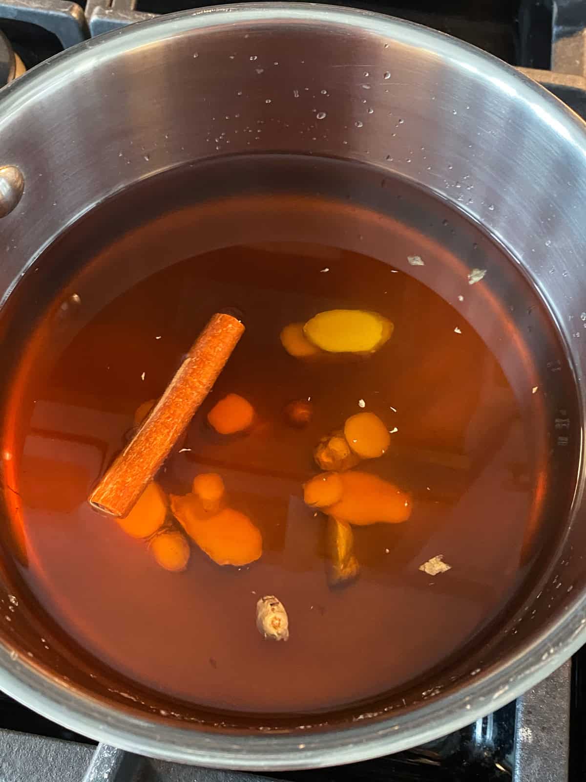 Vegetable stock in a pot, with a cinnamon stick and sliced ginger.