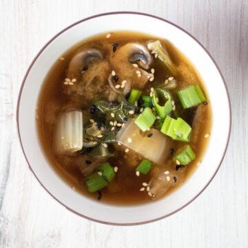 Overhead image of a bowl with bok choy and mushroom soup, garnished with sesame seeds.