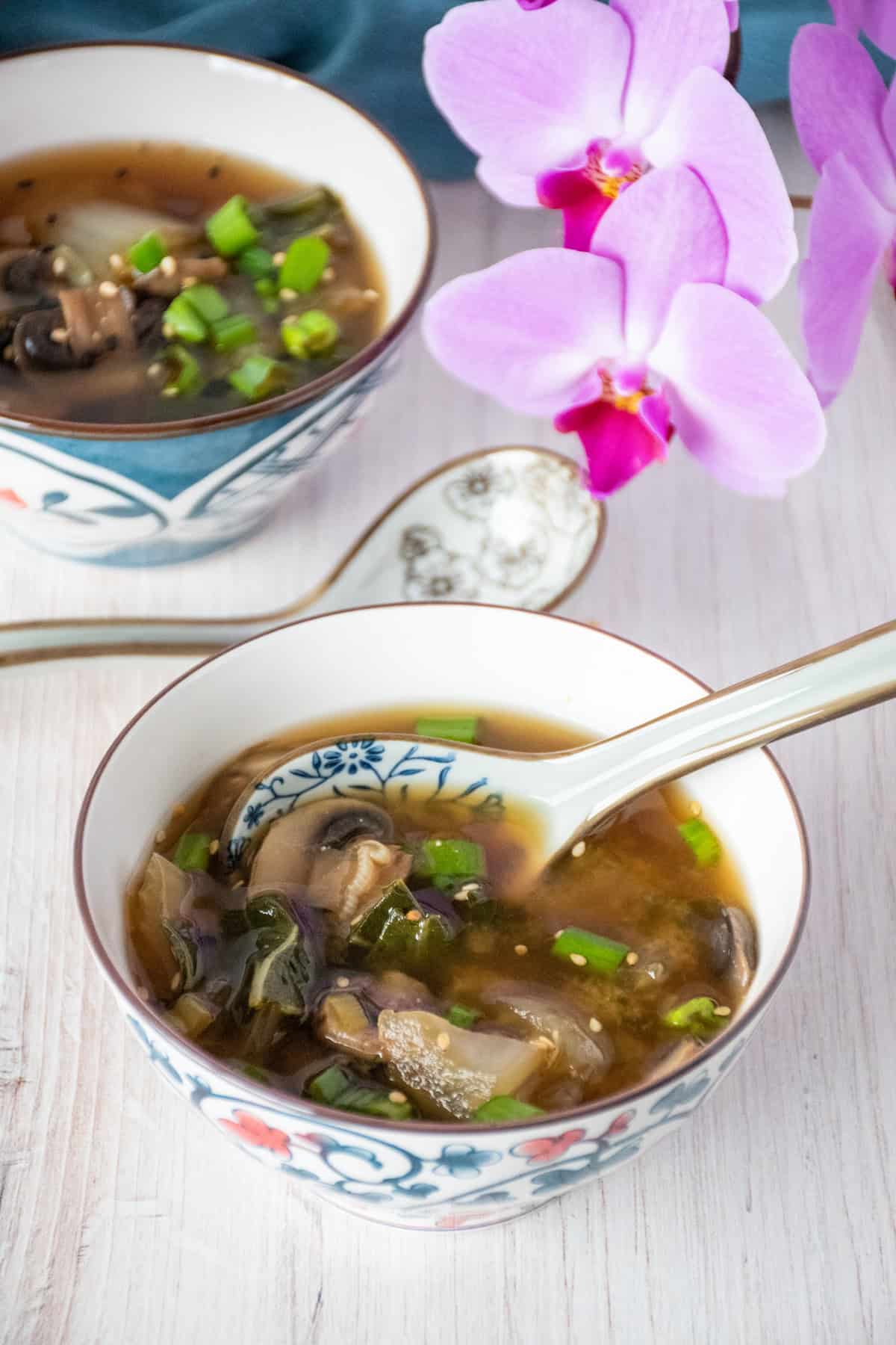Bowl with bok choy and mushroom soup, garnished with sesame seeds.