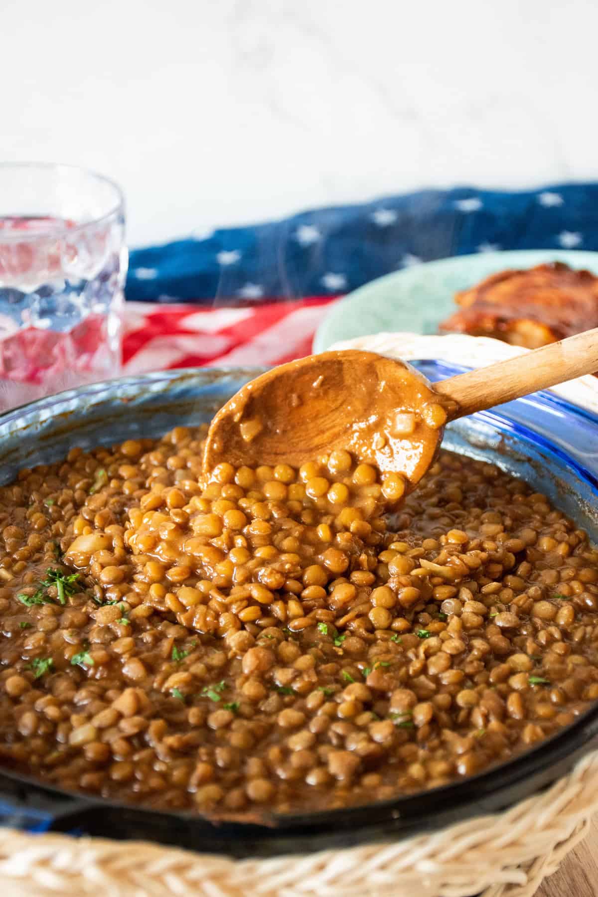 Glass baking dish with lentil baked beans and a wooden spoon scooping some.