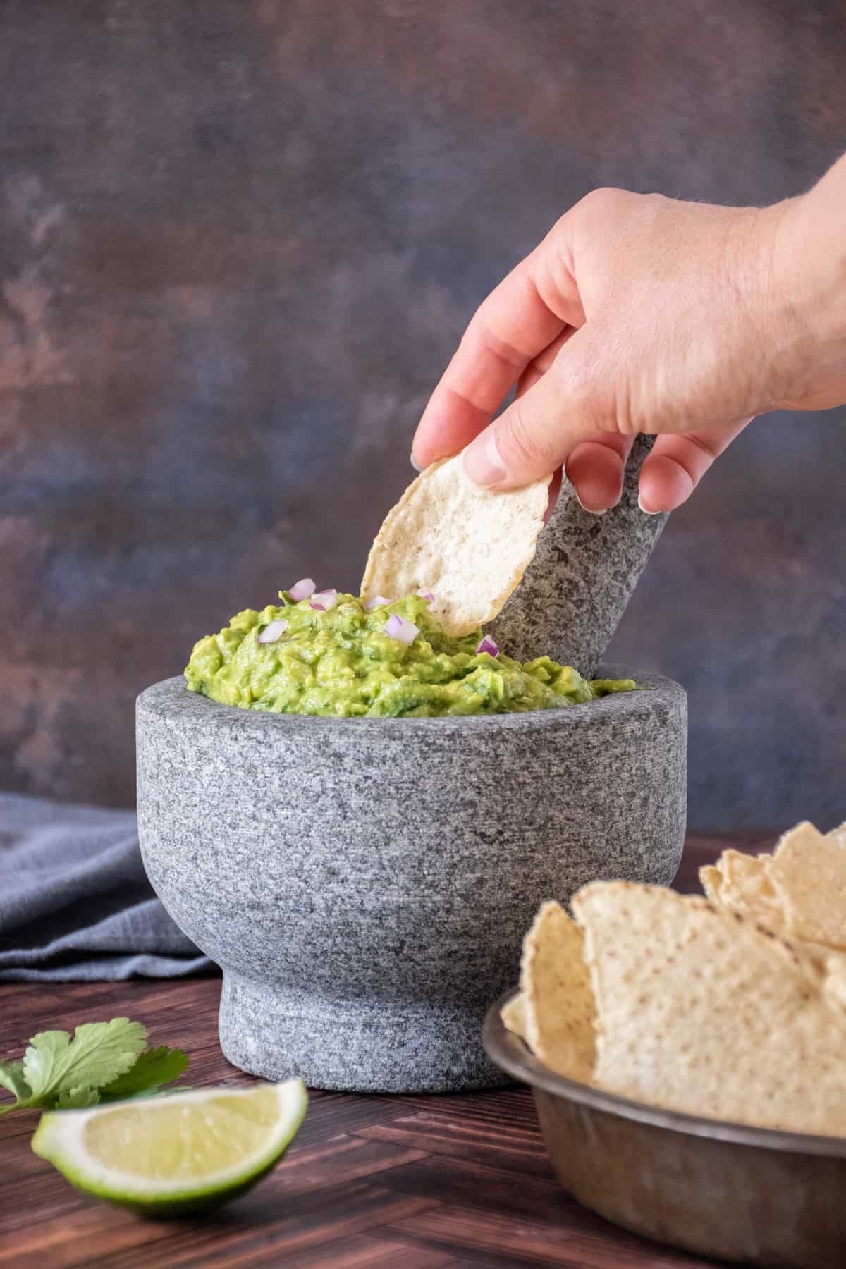 Large stone mortar and pestle filled with guacamole, with a tortilla chip being dipped into it.