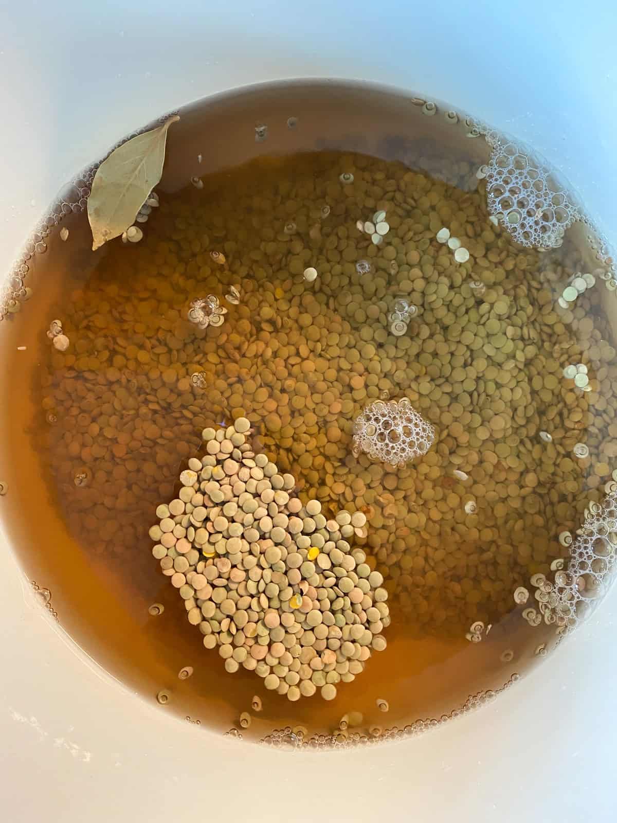 Dry lentils, vegetable stock, and bay leaf in a large pot, ready for cooking.