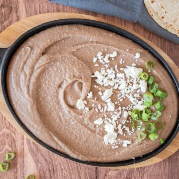 Refried beans in a small cast iron skillet, garnished with feta cheese and green onion slices.