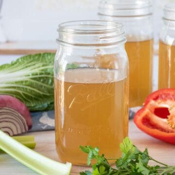 Vegetable stock in a mason jar, surrounded by fresh vegetables.