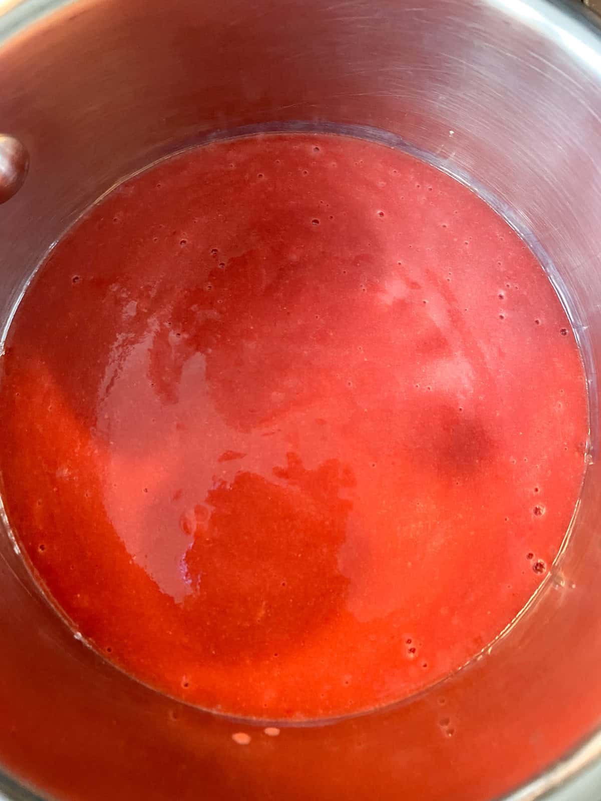 Blended strawberry sauce in a pan, simmering.