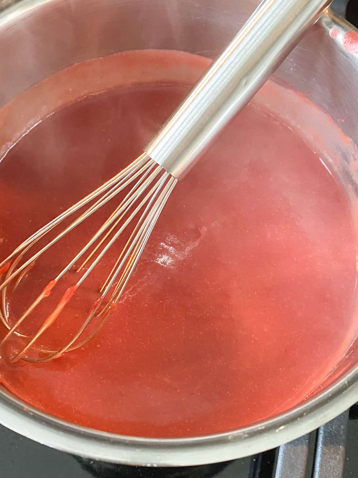 Reduced strawberry sauce in a pan with a whisk.