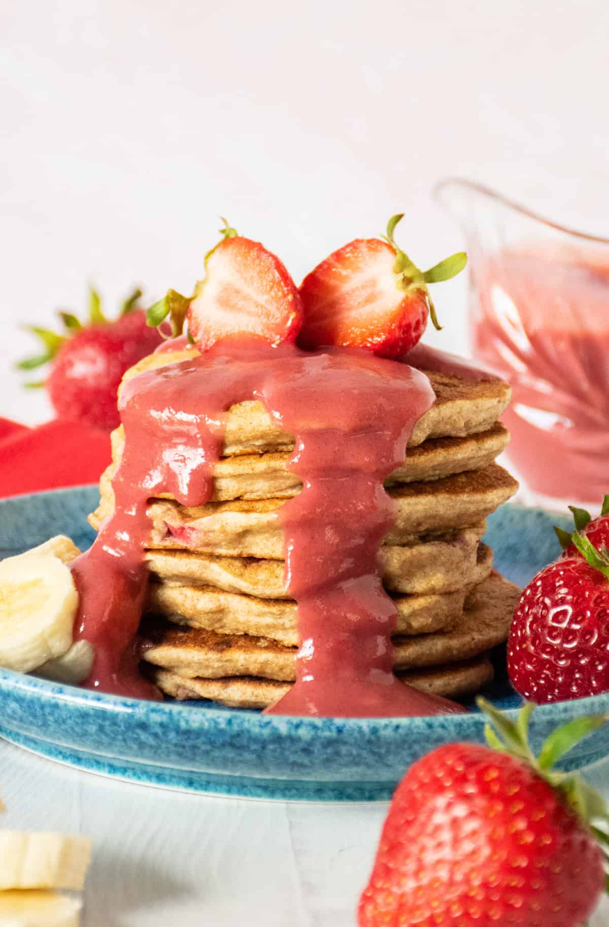 Stack of pancakes with strawberries on top, drizzled with strawberry sauce.